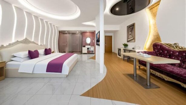 Een moderne hotelkamer met een gebogen plafond, een groot bed met hoofdeinde, een bank, een eettafel en een kitchenette.