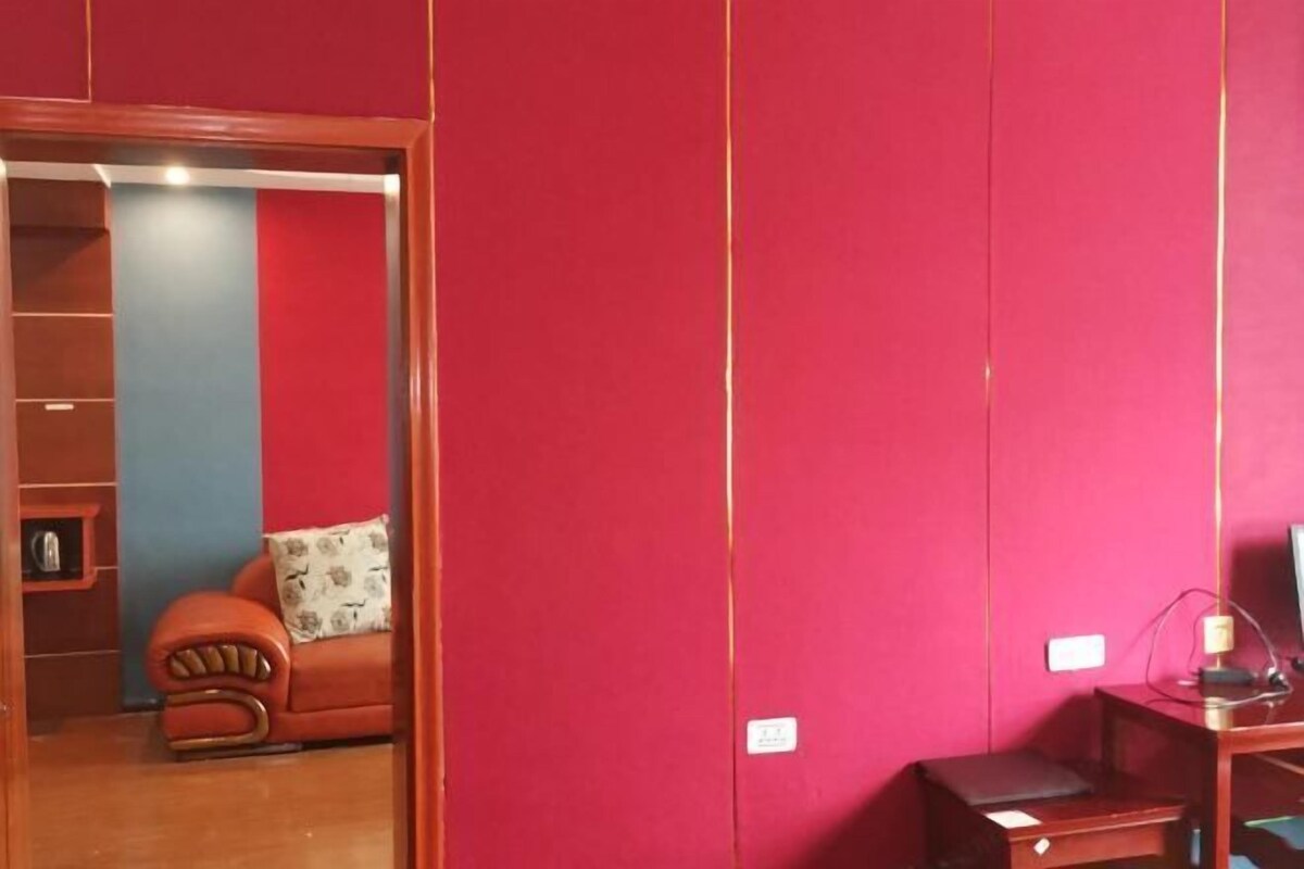 Une pièce avec un mur rouge, un meuble en bois, un canapé rouge orné d’un coussin à motifs et une petite table avec une lampe.