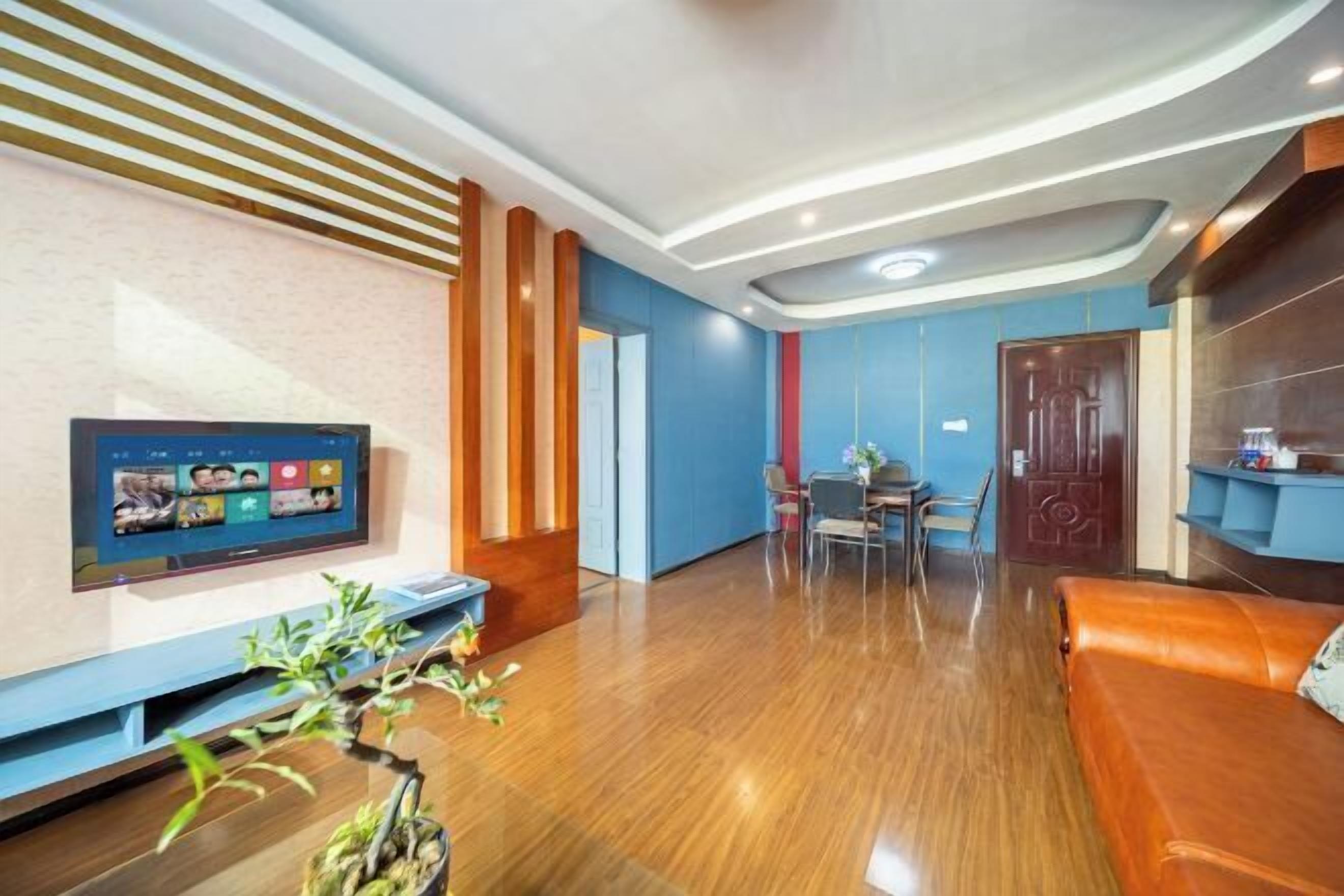 A modern living room with a flat-screen TV, wooden flooring, a leather sofa, and a dining area with chairs and a table.