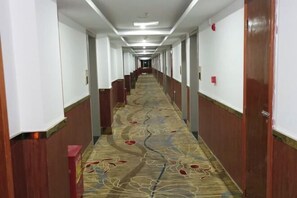 Un long couloir étroit, typique des hôtels, avec un tapis à motifs, des lambris en bois et une série de portes d’un seul côté.