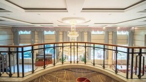 Een ruime lobby met een centrale kroonluchter, een gebogen balkonhek en uitzicht op de verdieping beneden.