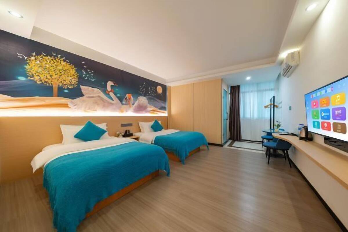 Hotelkamer met twee bedden, een muurschildering, een bureau met computer en een tv waarop diverse apps worden weergegeven.