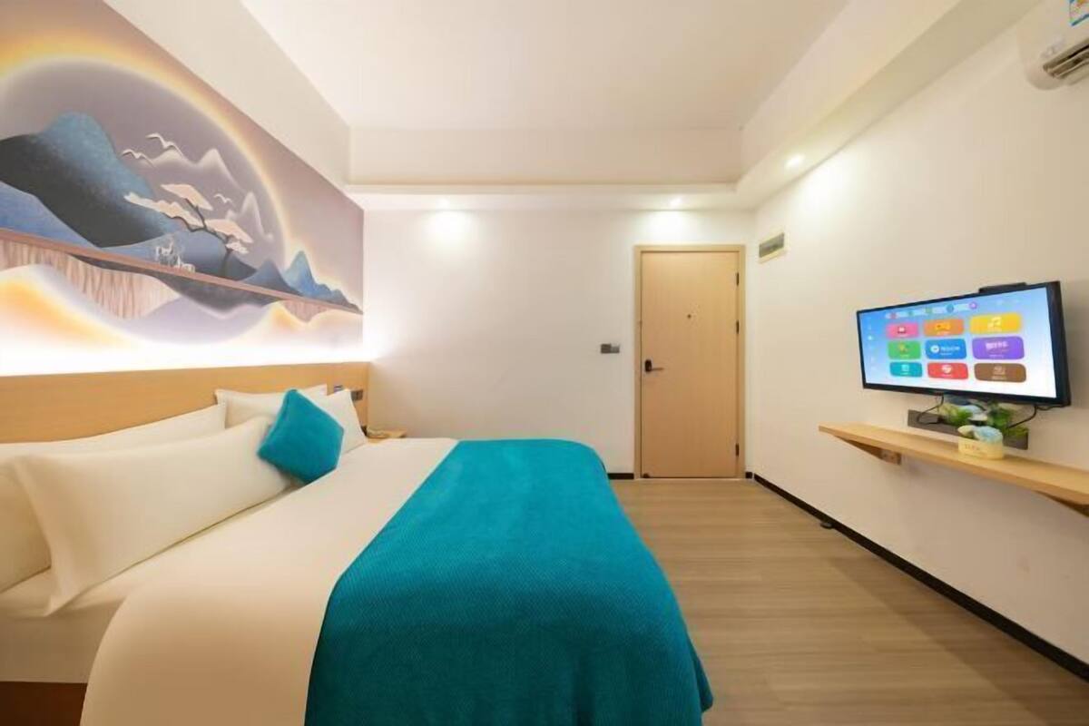 Een hotelkamer met een bed, een televisie op een standaard en een muurschildering.