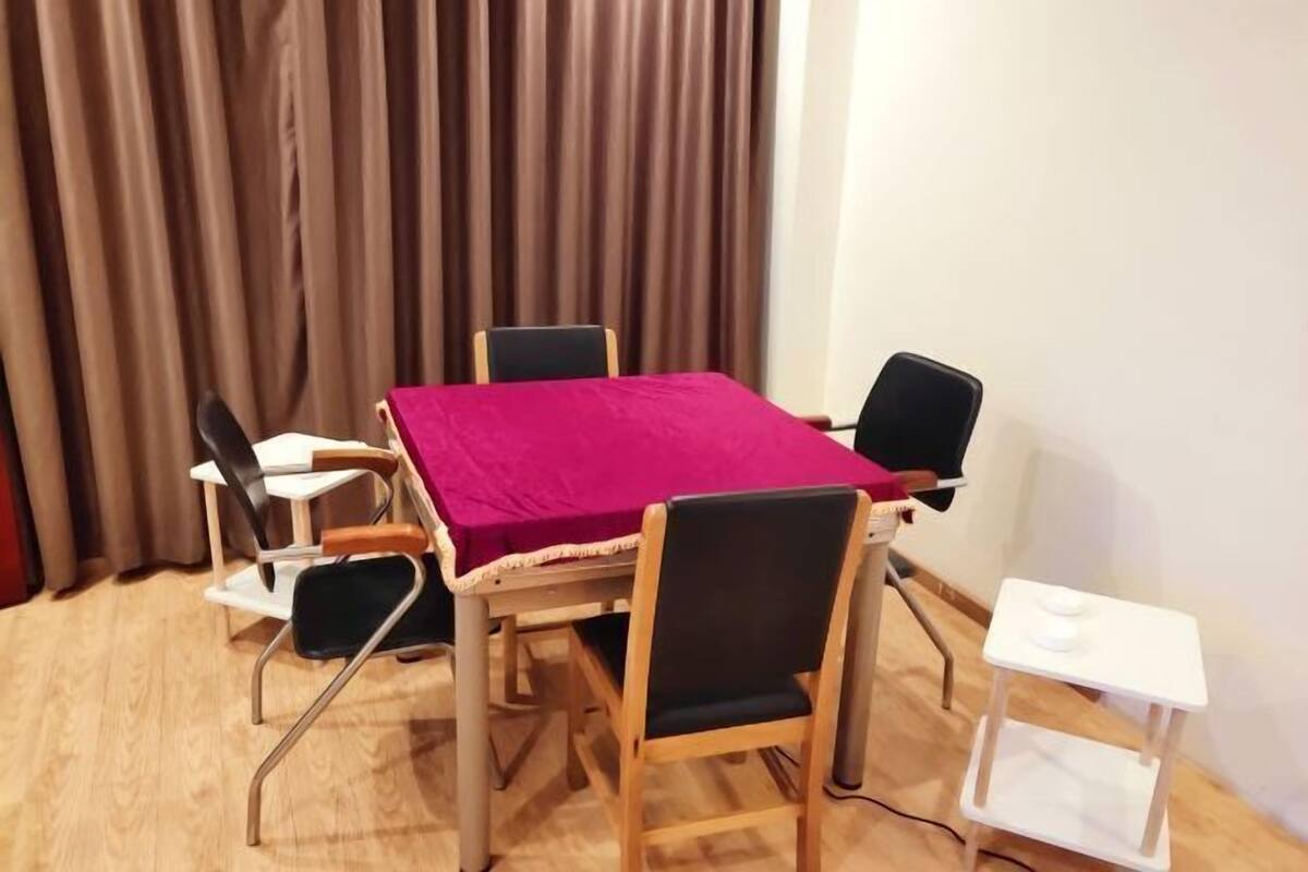 Een kamer met een houten tafel en stoelen, een rode tafelkleed, een witte bijzettafel en een gordijn op de achtergrond.