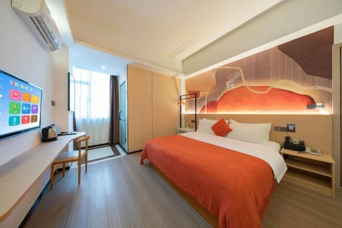 Een hotelkamer met een bed, een bureau, een stoel, een televisie en een kunstwerk aan de muur.