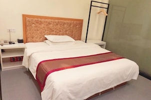 Habitación de hotel con una cama, una mesita de noche con un teléfono y una lámpara, y un perchero para toallas en la pared.