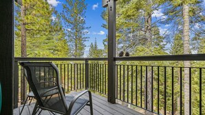 A wooden deck with a metal railing, a metal chair, and a view of tall pine trees. - Rocky Point #14 by Tahoe Getaways - HOA Pool, Gym, Tennis & More! (Truckee)