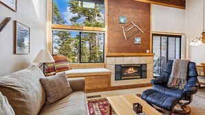 A cozy living room with a fireplace, a large window, and a comfortable seating area. - Rocky Point #14 by Tahoe Getaways - HOA Pool, Gym, Tennis & More! (Truckee)