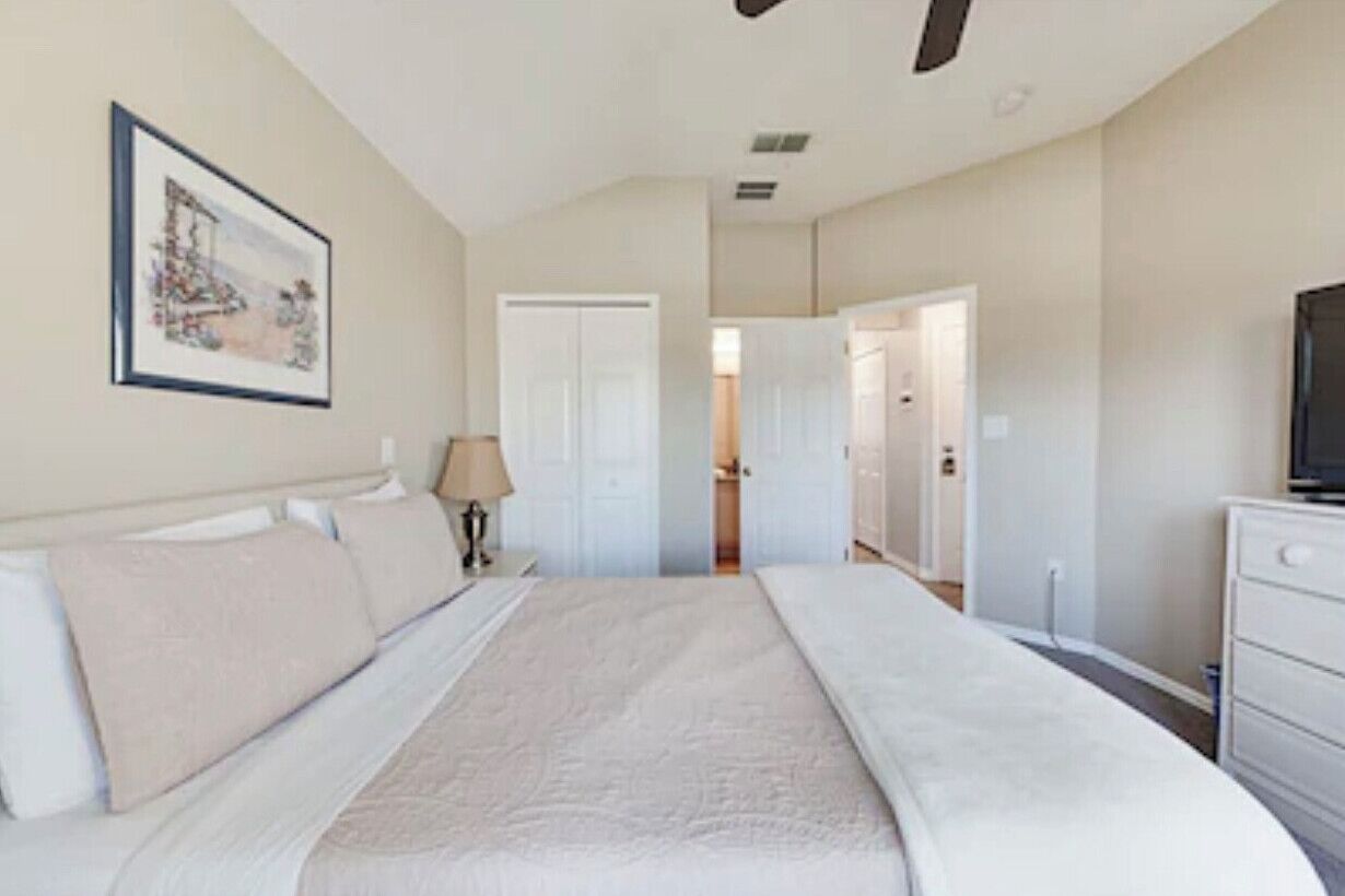 A bedroom with a bed, a TV, a dresser, and a door leading to another room.