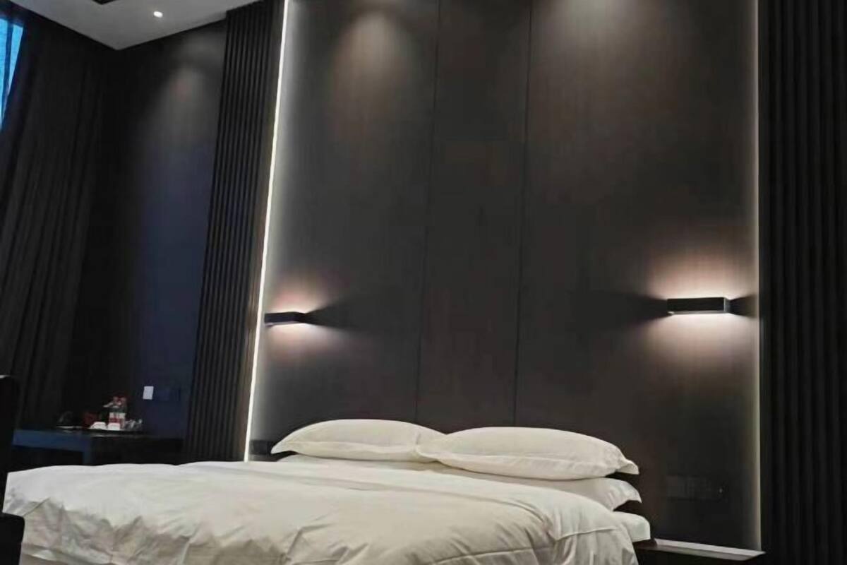 Una habitación de hotel moderna con una cama grande, paneles de madera oscura e iluminación empotrada.