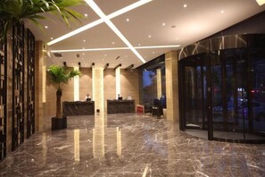 Un vestíbulo moderno con suelo de mármol, una recepción, una planta en maceta y una puerta de entrada de cristal.