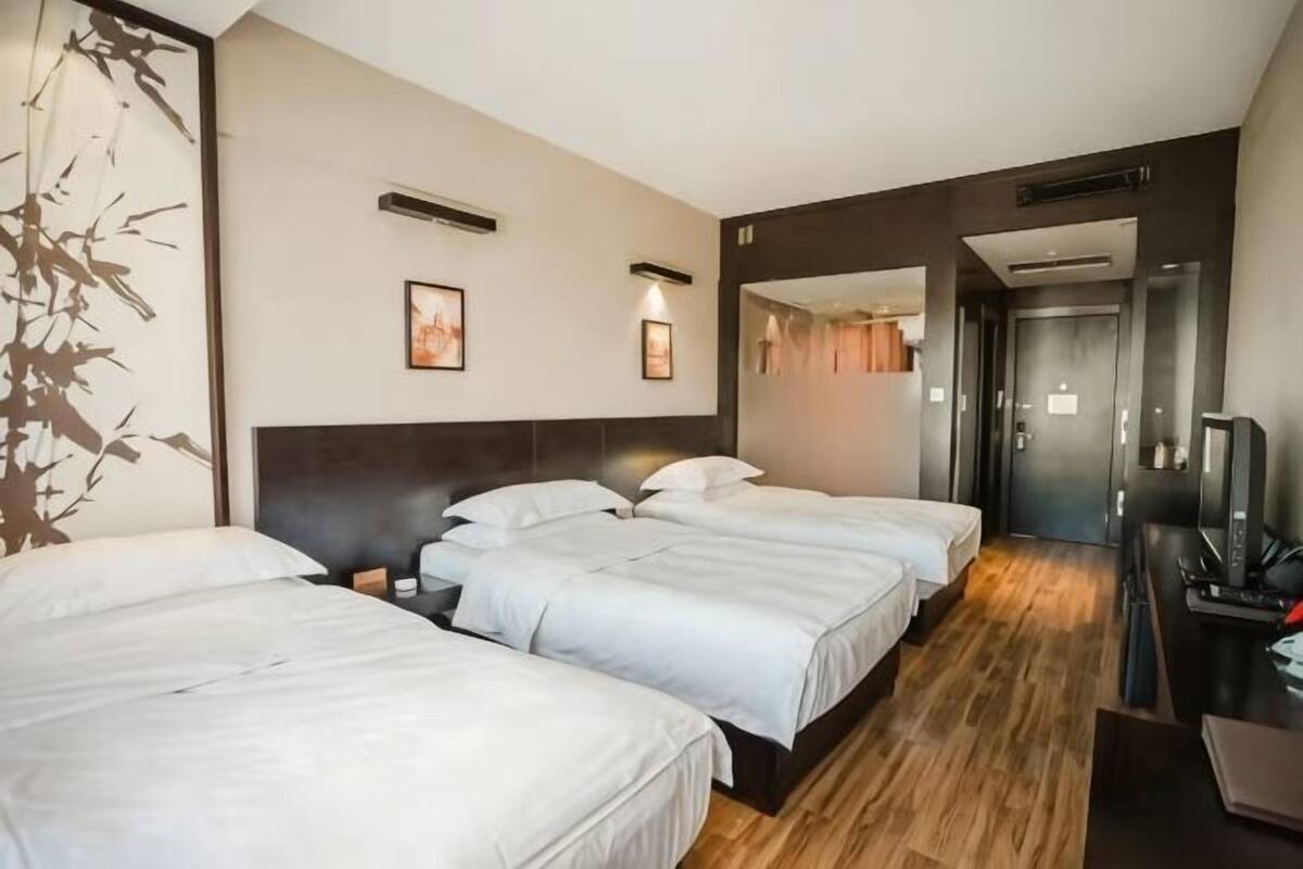 Habitación de hotel con tres camas, un escritorio con computadora y televisión.