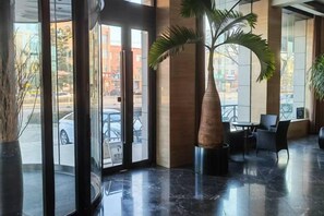 A lobby with a palm tree, a seating area, and a view of the street. - Yongsheng Business Hotel (Jianping)