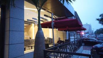 A modern building with a glass facade, outdoor seating area, and a palm tree.