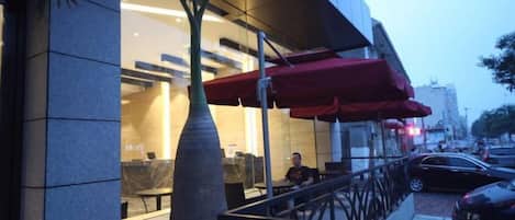 A modern building with a glass facade, outdoor seating area, and a palm tree.