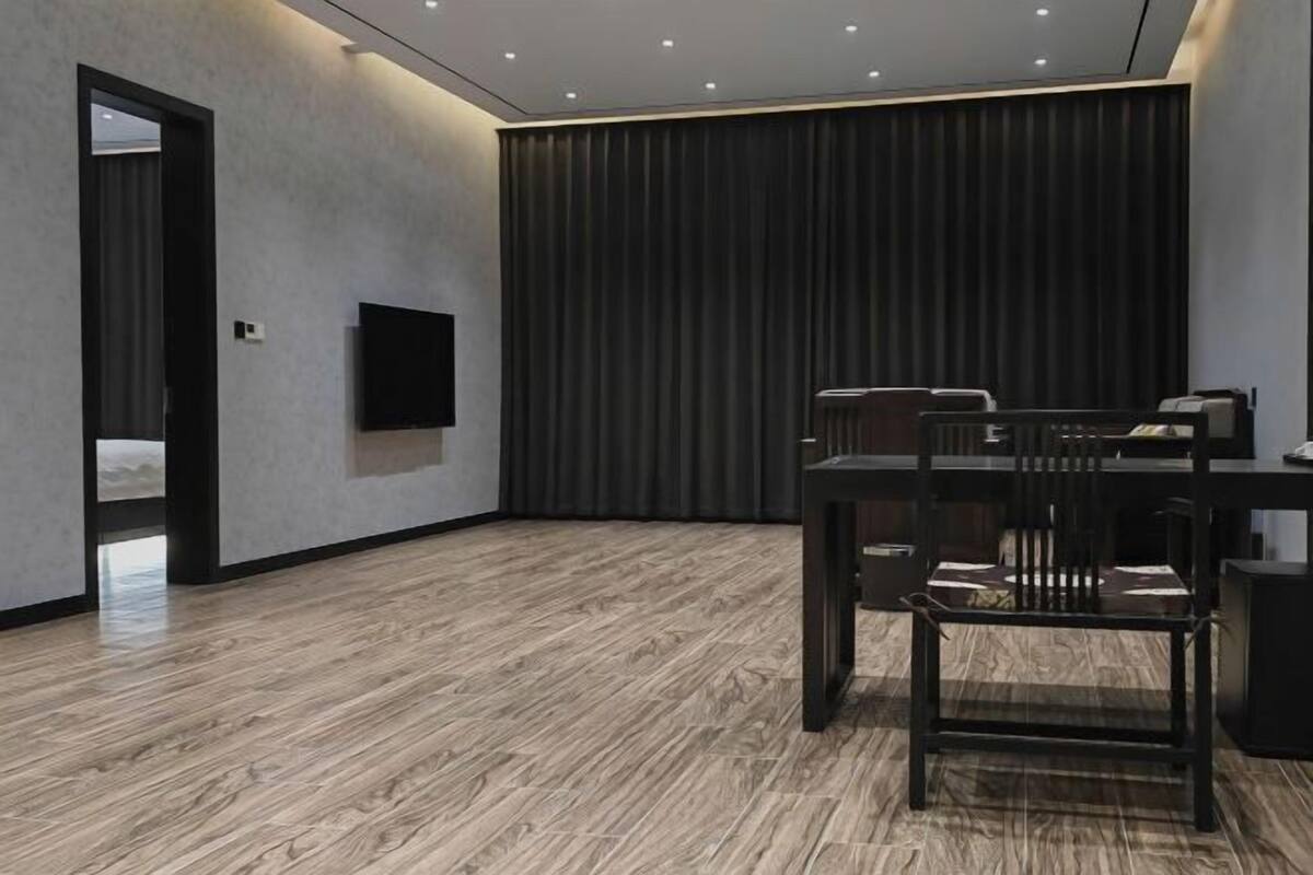 Una habitación moderna con piso de madera, un televisor de pantalla plana en la pared, una cortina oscura y una mesa con sillas.