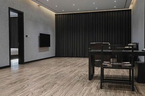 Een moderne kamer met een houten vloer, een flatscreen televisie aan de muur, een donker gordijn en een tafel met stoelen.