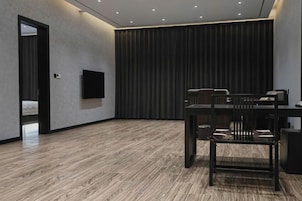 Una habitación moderna con piso de madera, un televisor de pantalla plana en la pared, una cortina oscura y una mesa con sillas.
