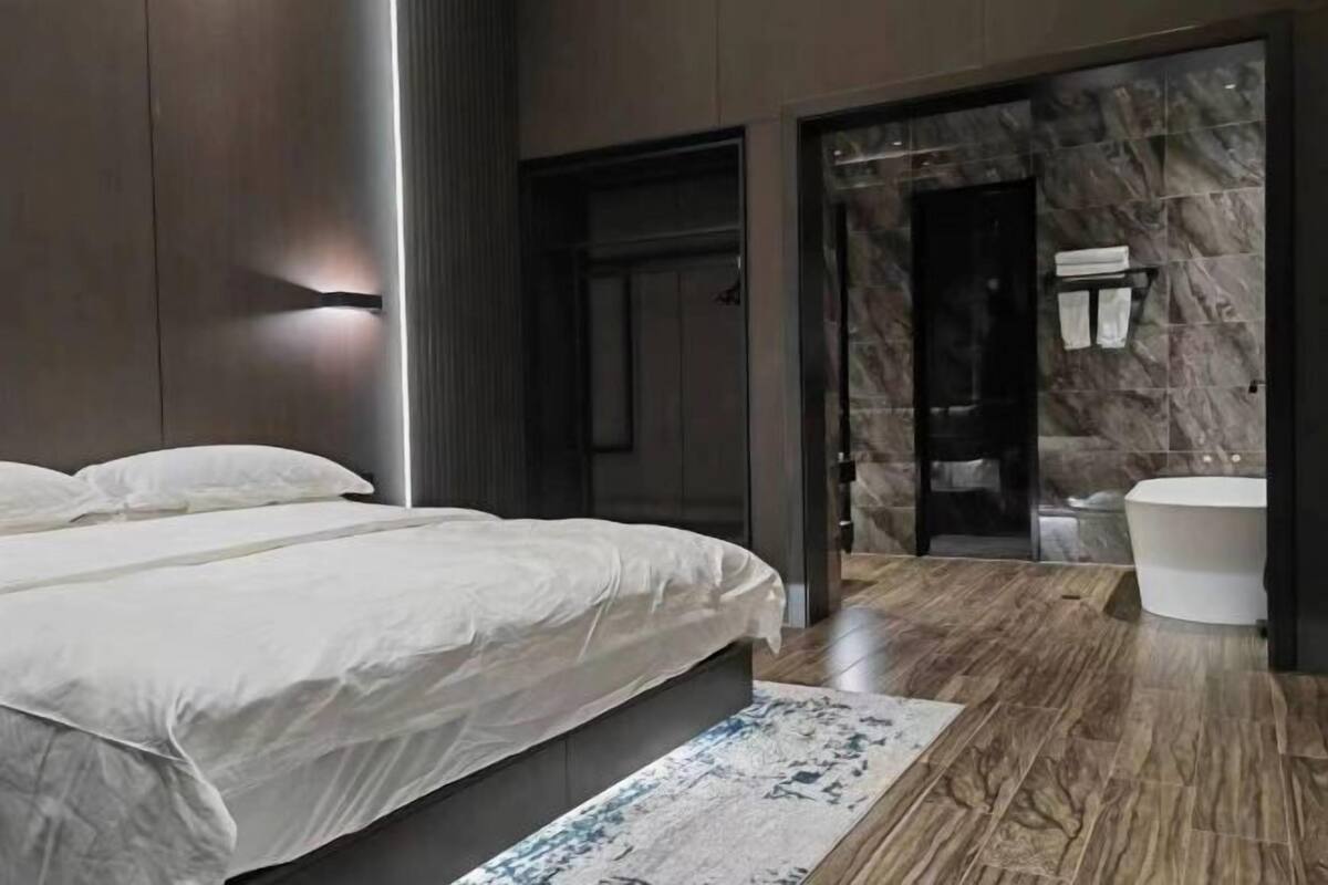 Un dormitorio moderno con una cama grande, un baño con pared de mármol y suelo de madera.