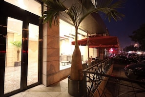 An outdoor seating area with a palm tree, a red umbrella, and a view of the street. - Yongsheng Business Hotel (Jianping)