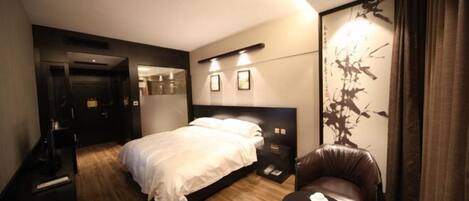 A modern hotel room with a large bed, a sitting area with a table, and a wall-mounted artwork.