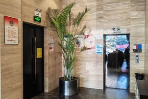 Un ascensor con un cartel que indica que es para vehículos eléctricos, una planta en maceta y un cartel fijado a la pared con texto.