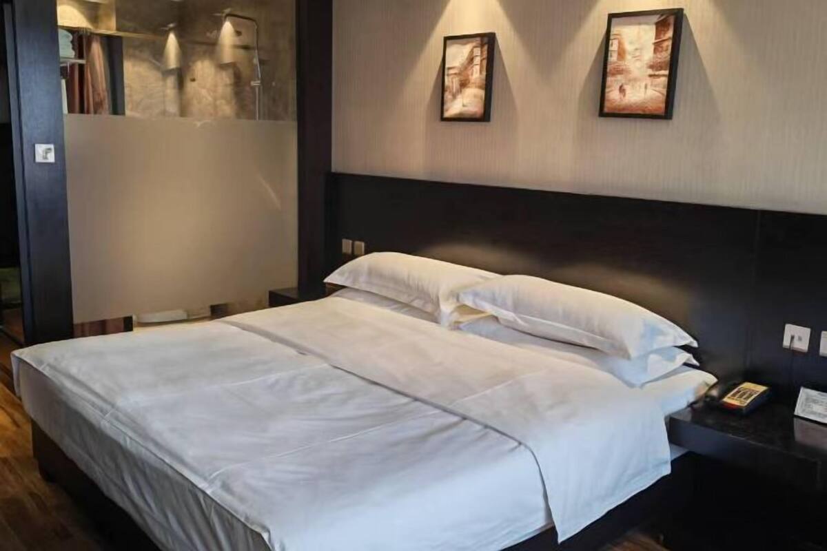 Habitación de hotel con una cama grande, una mesita de noche con lámpara y dos cuadros enmarcados en la pared.