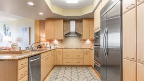 A modern kitchen with wooden cabinets, stainless steel appliances, and a patterned rug. - Cozy Three Bedroom Bayside Unit with Gorgeous Bay Views! Complimentary Boat Slip! (Orange Beach)