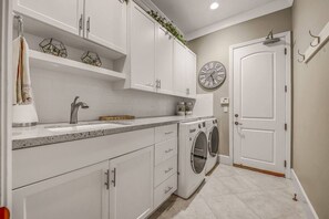 A modern kitchen with white cabinetry, a built-in washing machine, a sink, and a clock on the wall. - Palm Oasis: Pool, Spa, Putting Green, BBQ! (Indio)