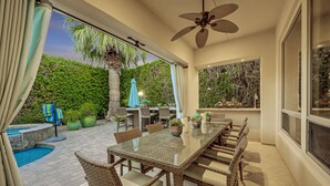 A spacious patio with a glass-top dining table, wicker chairs, and a ceiling fan. - Palm Oasis: Pool, Spa, Putting Green, BBQ! (Indio)