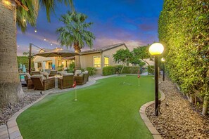 A well-maintained lawn with a putting green, outdoor furniture, and a house with a patio. - Palm Oasis: Pool, Spa, Putting Green, BBQ! (Indio)