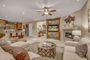 A spacious living room with a fireplace, a television, and a ceiling fan.