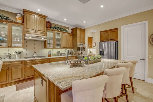 A kitchen with wooden cabinets, a stainless steel refrigerator, and a large island with bar stools.