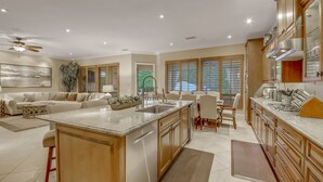 A spacious kitchen with a central island, wooden cabinets, and a dining area with a table and chairs. - Palm Oasis: Pool, Spa, Putting Green, BBQ! (Indio)