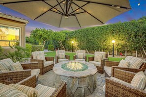 Un patio al aire libre con mobiliario de mimbre, una chimenea de piedra y un paraguas grande.