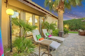 A patio area with lounge chairs, a palm tree, and string lights.