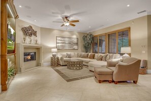 A spacious living room with a fireplace, a large sectional sofa, a coffee table, and a ceiling fan.
