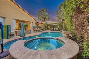 A swimming pool with a hot tub, surrounded by a patio area with outdoor furniture and a view of a house. - Palm Oasis: Pool, Spa, Putting Green, BBQ! (Indio)