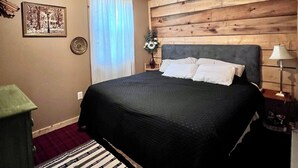 Une chambre avec un plafond en bois, un lit avec des oreillers blancs, une table de chevet avec une lampe et une fenêtre avec des rideaux.