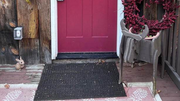 Une porte rouge avec un cadre blanc, une boîte aux lettres, une pancarte indiquant «Vers le chalet», une guirlande et un paillasson.