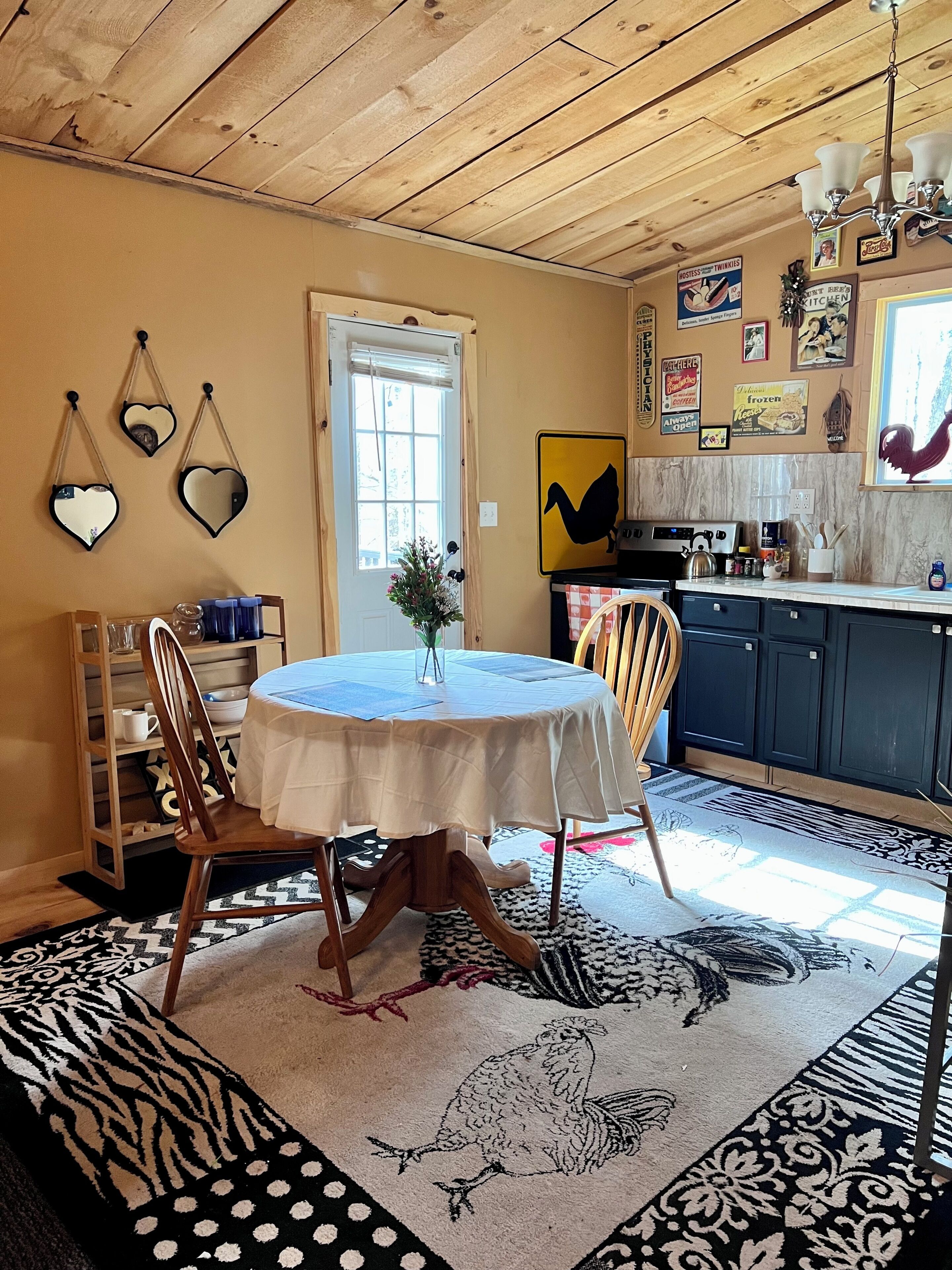 Un comedor con una mesa redonda, sillas, una cocina al fondo y una puerta con ventanal.