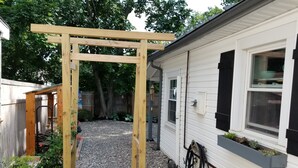 A wooden arbor in a backyard with a gravel path, potted plants, and a white mobile home. - That Cottage by the Lake!! (Canandaigua)