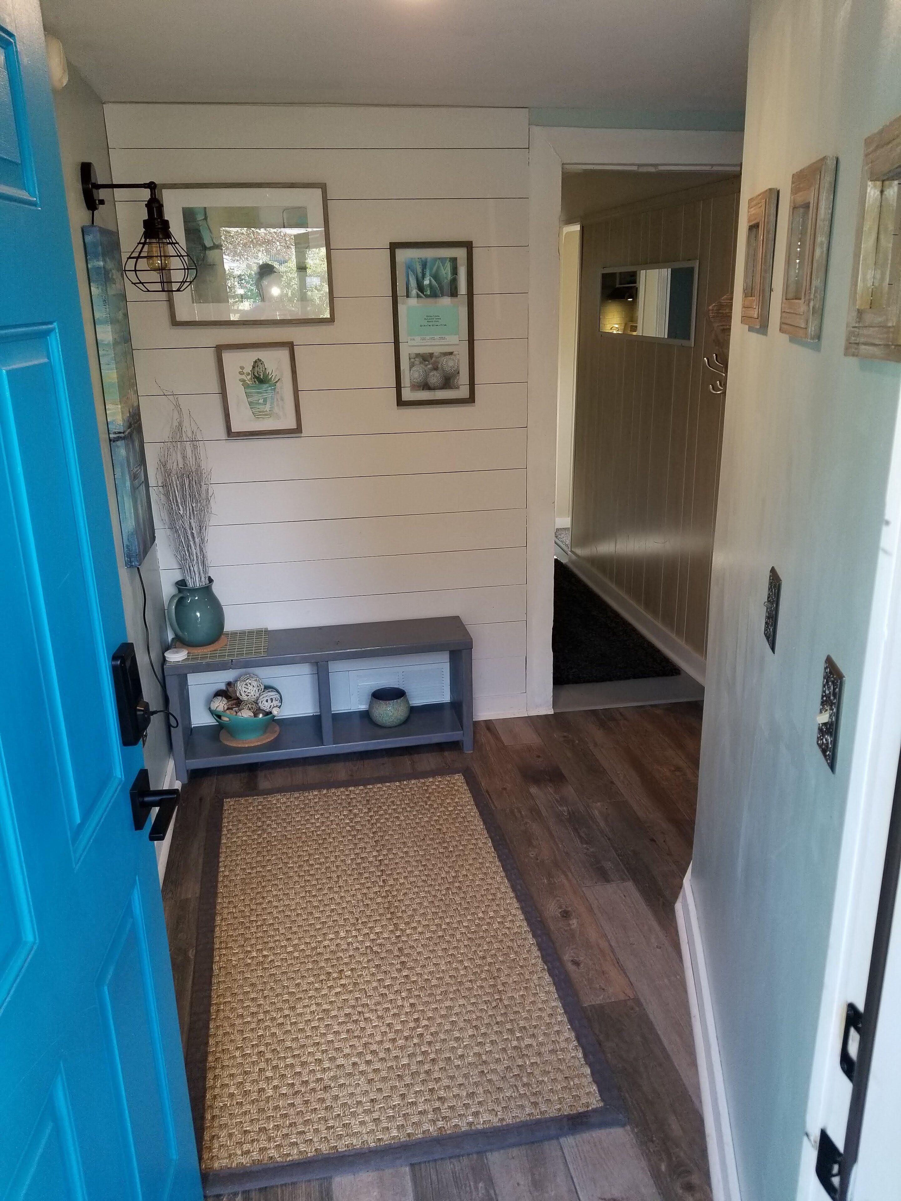 A hallway with a blue door, a woven rug, a console table with decorative items, and framed artwork on the wall.