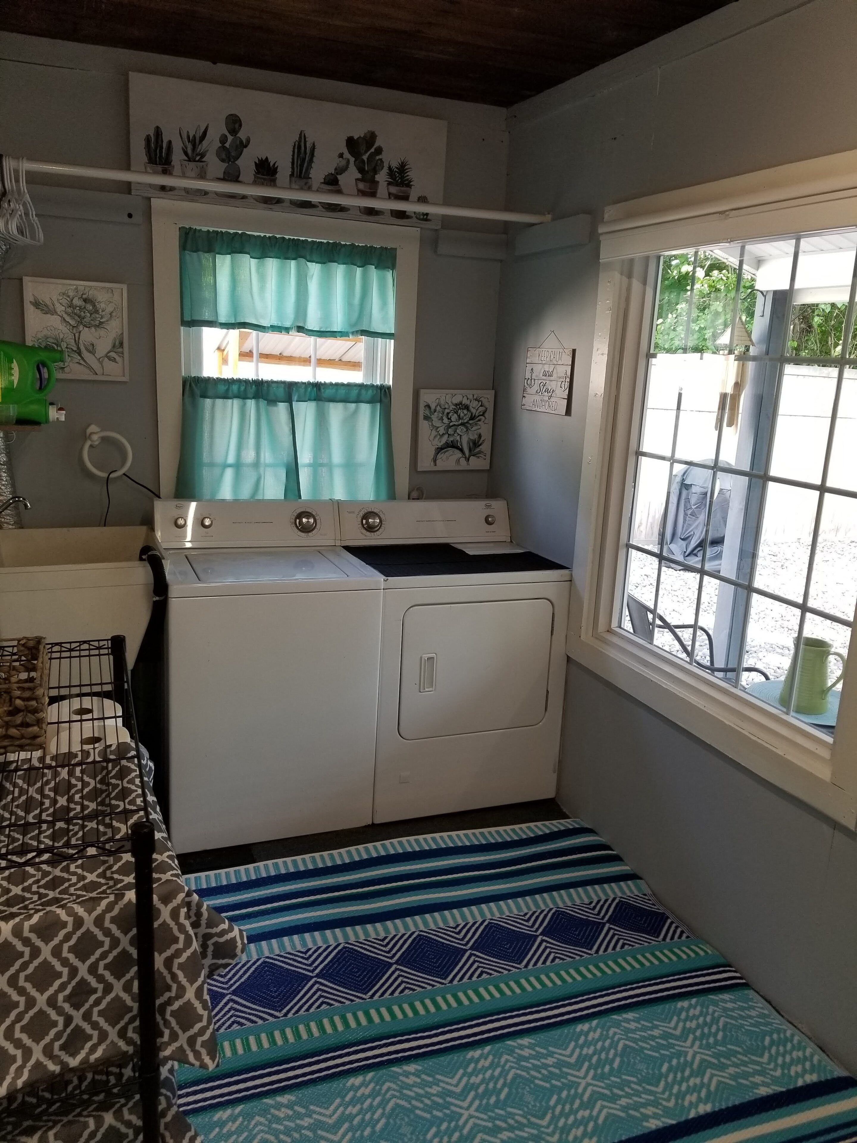A compact laundry room with a washing machine, drying rack, and a window with a view of the outside.