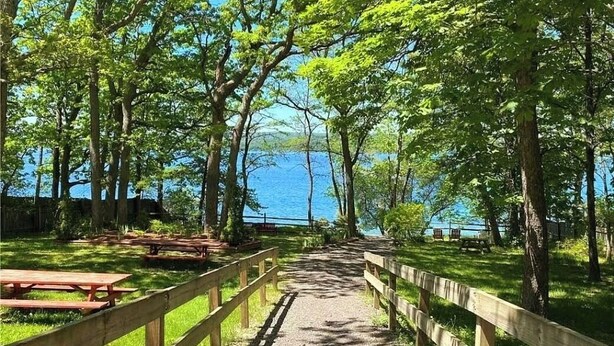 A pathway lined with wooden benches leading to a body of water, surrounded by trees. - That Cottage by the Lake!! (Canandaigua)