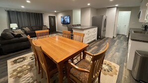 A modern living room with a dining table and chairs, a sofa, a TV, and a kitchen area with a refrigerator. - NEW, Super Comfortable Ranch! (Mentor)