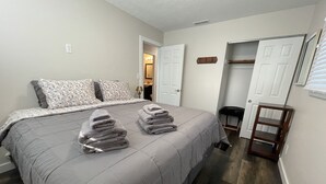 A neatly made bed with a grey duvet and two pillows, a wooden bench, and a door leading to a bathroom. - NEW, Super Comfortable Ranch! (Mentor)