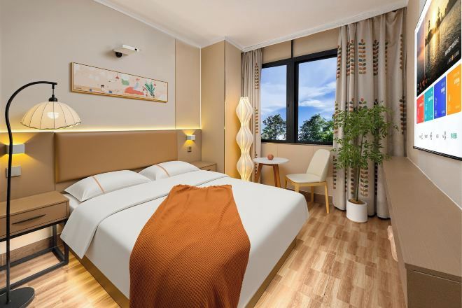 A hotel room with a bed, bedside table, lamp, chair, potted plant, and a window with curtains.