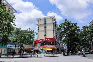 A multi-story building with a red sign, a pedestrian area with benches, and a clear sky. - Youran Crazy Hotel (Gongbei Xiawan Branch) (Zhuhai)