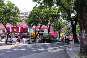 A street with parked cars, trees, and buildings with signage. - Youran Crazy Hotel (Gongbei Xiawan Branch) (Zhuhai)